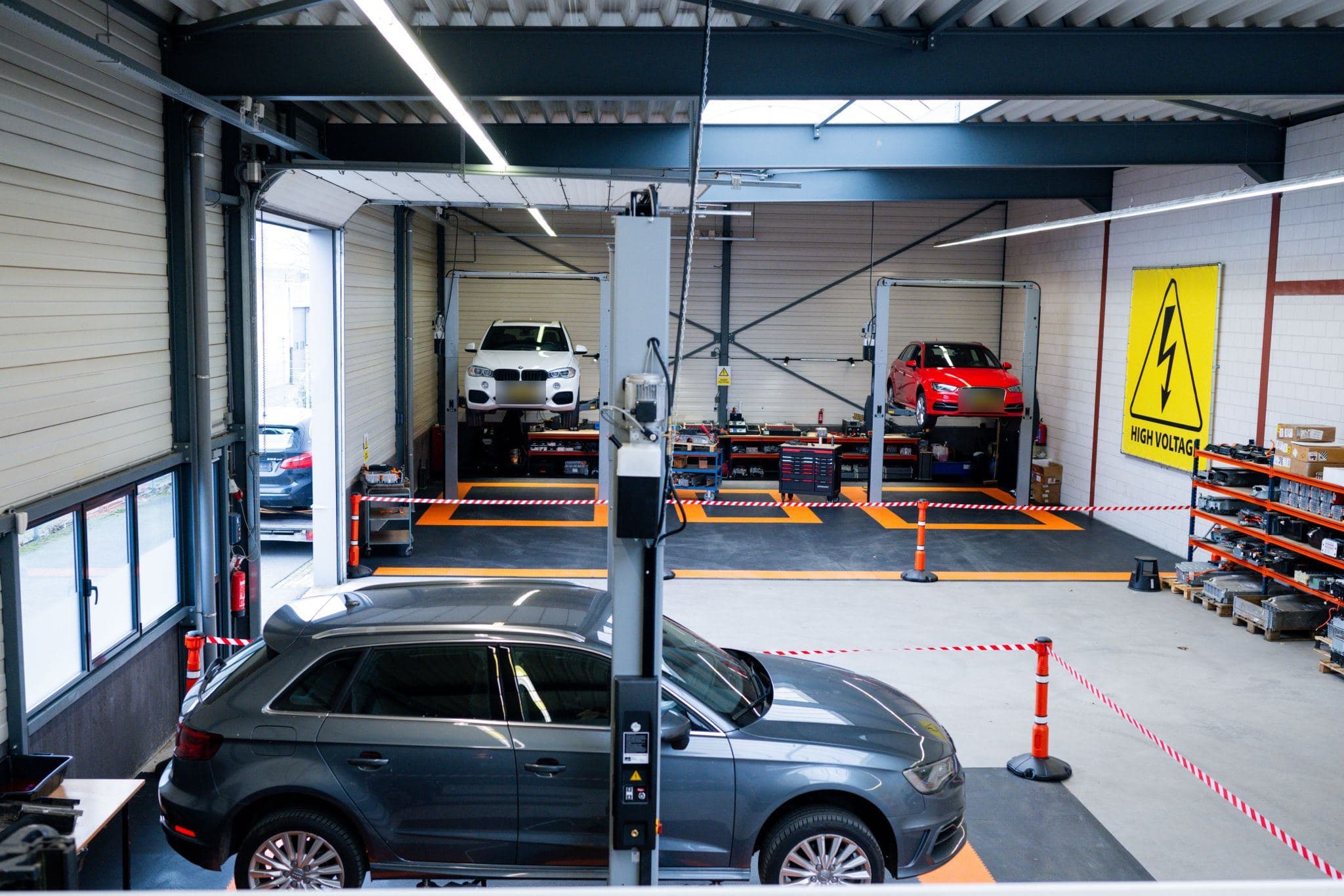 De werkplaatshal met twee bruggen, werkbanken met accumodules en een HIGH VOLTAGE-bord.